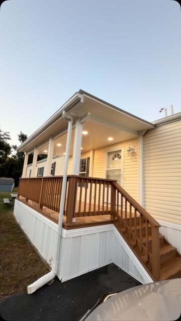 A stained wood deck with railings and stairs along a cream-sided home, a new white awning overhead with lights glowing at dusk.